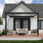 Backyard Discovery Evanston 12 x 10 ft. black steel louvered pergola mounted to a white brick house